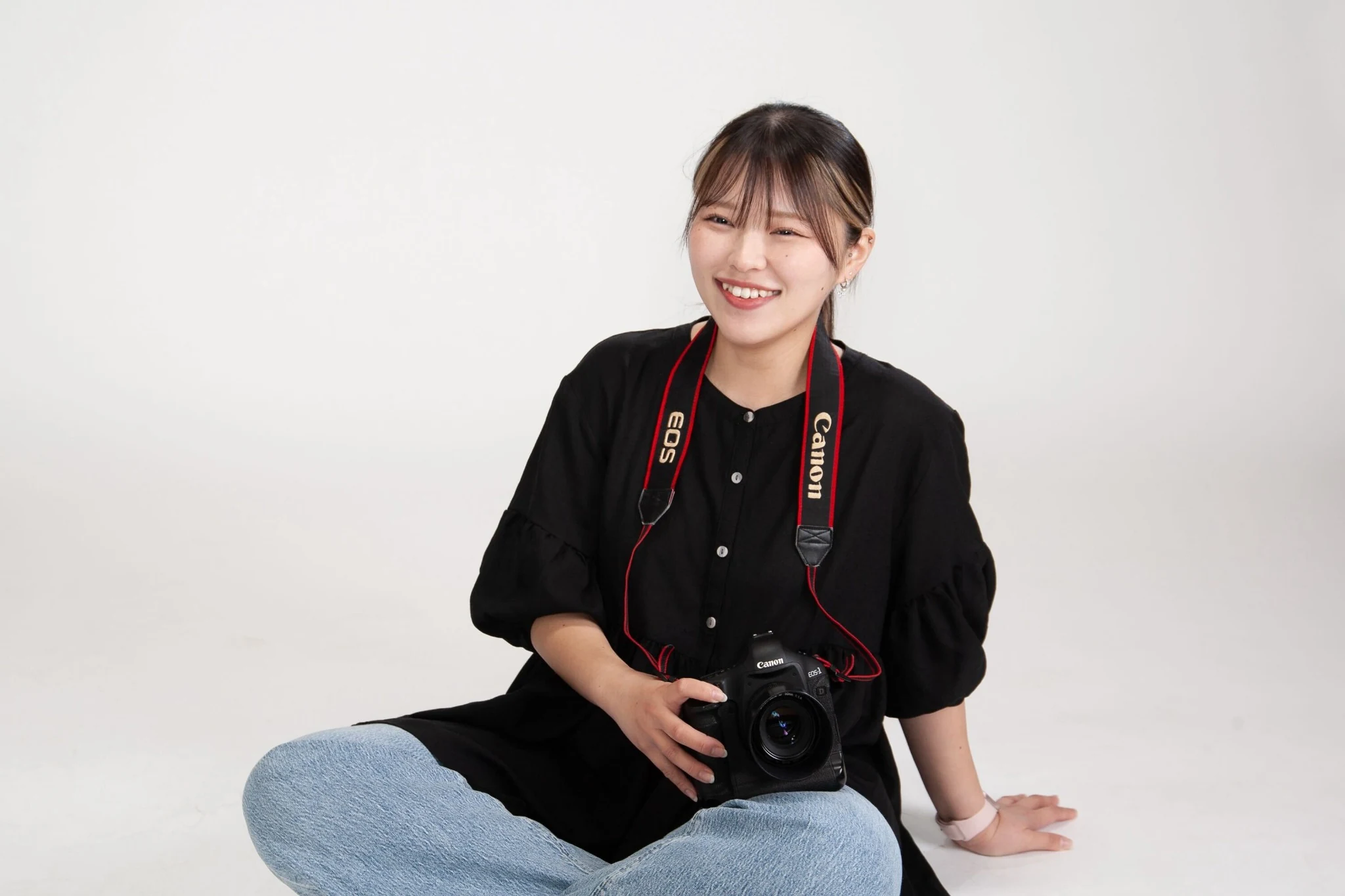 小林 伽奈さんのプロフィール写真。カメラを持って白背景で座っている様子